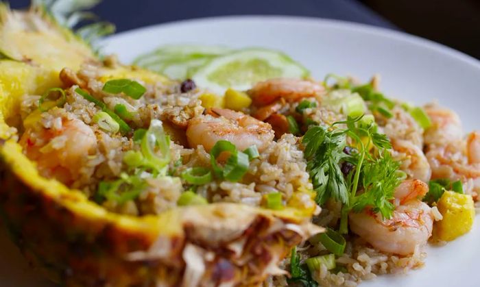 A vibrant pineapple hollowed out and generously filled with shrimp, rice, and fresh herbs, served on a large plate.