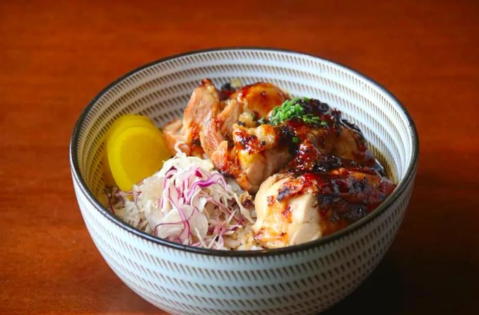 A bowl featuring rice, succulent grilled chicken, and tangy pickled vegetables.