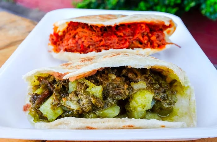 A gordita filled with bright red meat, another with green salsa verde meat, all served on a white rectangular plate.