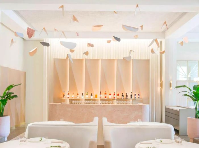 A bright and airy restaurant interior adorned in white, featuring mobiles suspended above tables dressed in white tablecloths.