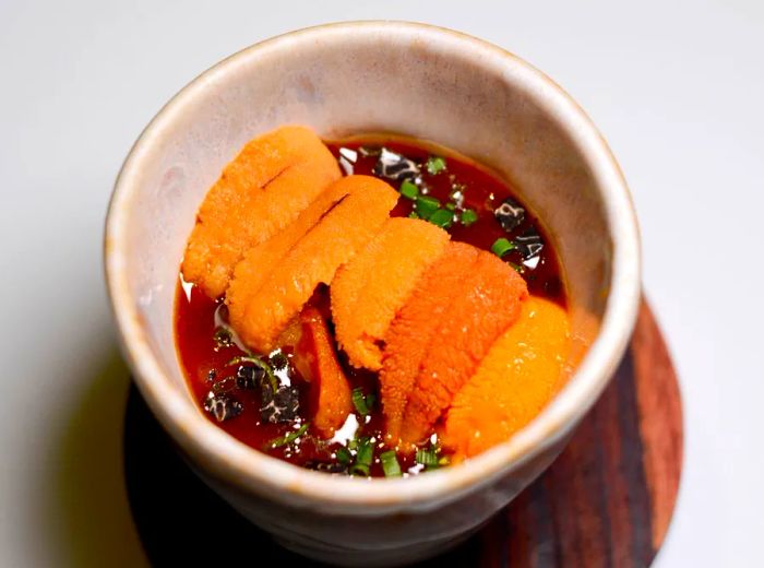 A small clay bowl of gyeran jjim garnished with generous pieces of uni.