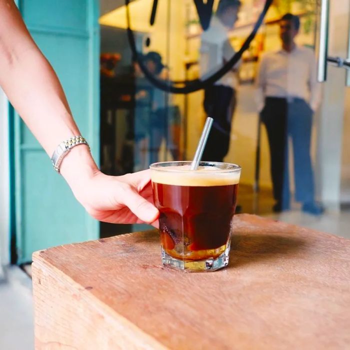 A customer reaches for a frothy coffee drink from the counter.