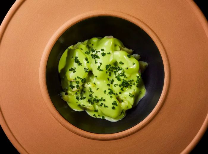 A bronze dish featuring a vibrant green dish at its center.