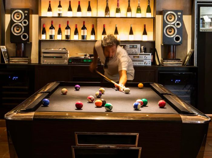 A player enjoys a game of pool in front of a large, backlit wall of bottles.