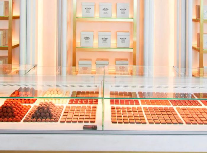 An elegant display of pastries with boxes showcased on an arching wall and a glass case revealing even more delicious treats.