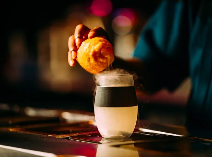 A bartender releases a cloud of smoke from a hollowed lemon into a cocktail.