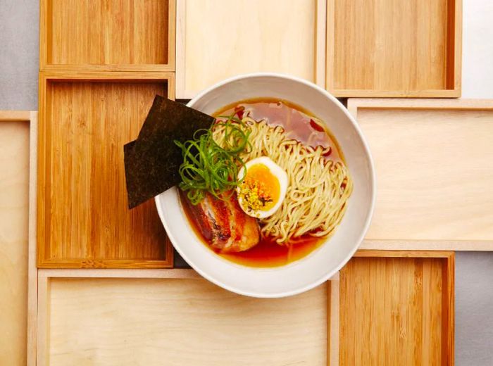 An overhead view of a ramen bowl brimming with noodles, a soft-boiled egg, fresh greens, slices of pork, and sheets of nori.