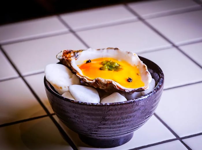 A sizable shell holds a creamy yellow dish, presented on a patterned tile surface.