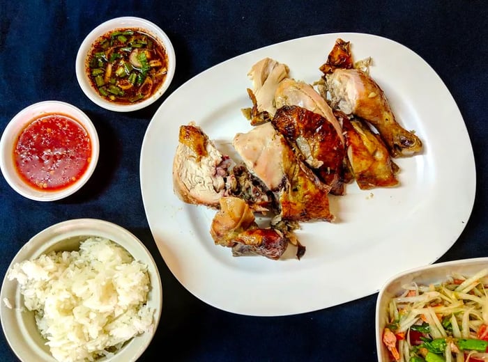 A platter of succulent rotisserie chicken served with sticky rice, a fresh side salad, and various dipping sauces on a dark table