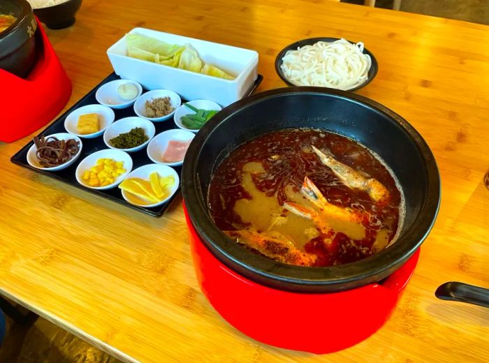 A steaming bowl of broth accompanied by noodles and various add-ins.