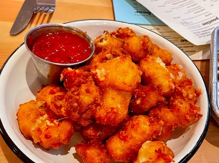 A serving of crispy fried cheese curds accompanied by a dipping sauce.