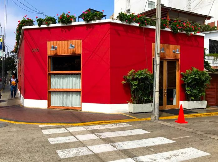 An exterior view of Rafael Restaurant, a charming, single-story red building located on a street corner, with a small garden and plants decorating the rooftop edge.