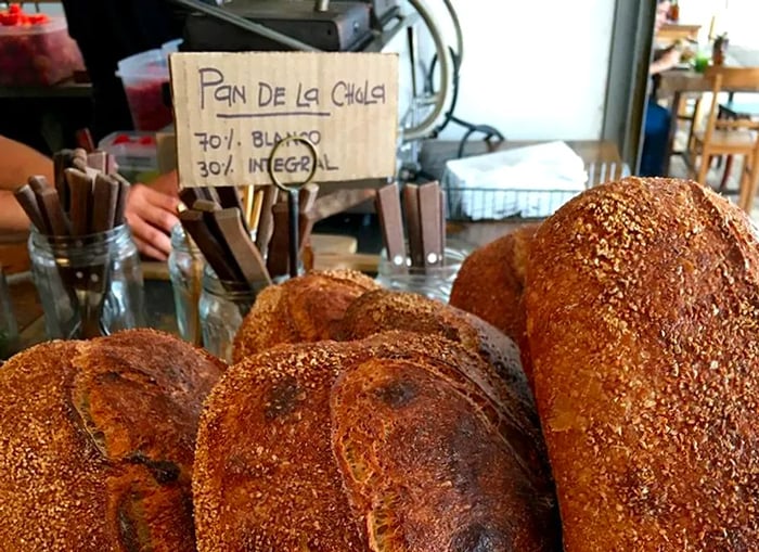 Artisan loaves are displayed on a café counter, with a hand-written price list nearby.