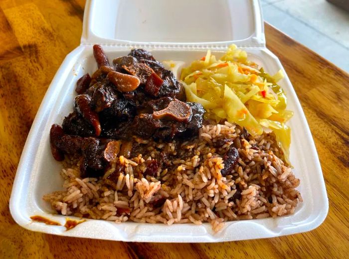 A takeout box filled with tender oxtail served with rice, peas, and cabbage.