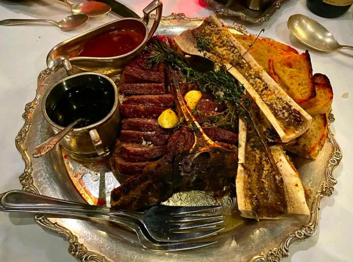 A luxurious bone-in steak, complete with bone marrow and an array of sauces, elegantly served on a silver platter.