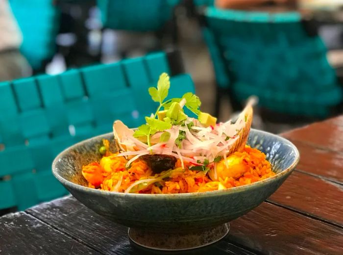 A vibrant bowl of ceviche, brimming with large chunks of fish and topped with a fresh herb sprig, rests on an outdoor table next to a patio chair.