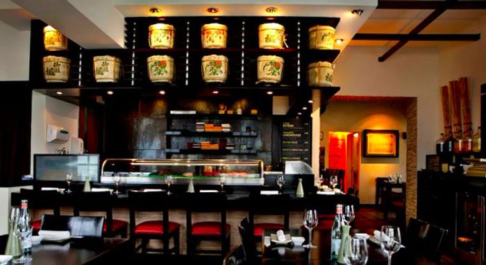 A bar area adorned with glowing sake casks overhead, complemented by several dining tables in the background.