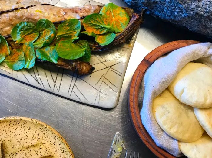 A beautifully garnished fish, adorned with a row of fresh herbs, is presented alongside a bowl of fluffy, freshly-made arepas.