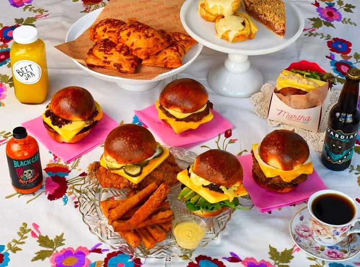 A colorful spread featuring burgers, sandwiches, fries, drinks, and more set atop a floral tablecloth.