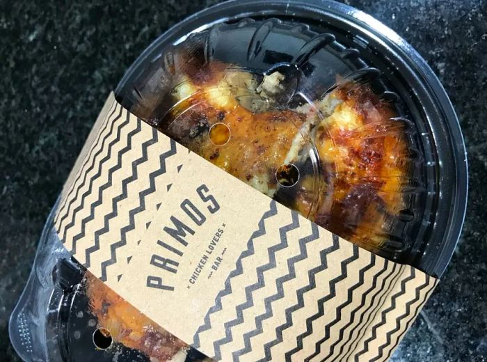 A whole roasted chicken packaged in a plastic container featuring the Primos Chicken Bar logo.