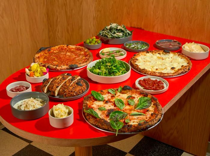 A table covered with an array of pizzas, salads, breads, and side dishes, set against a red tablecloth.