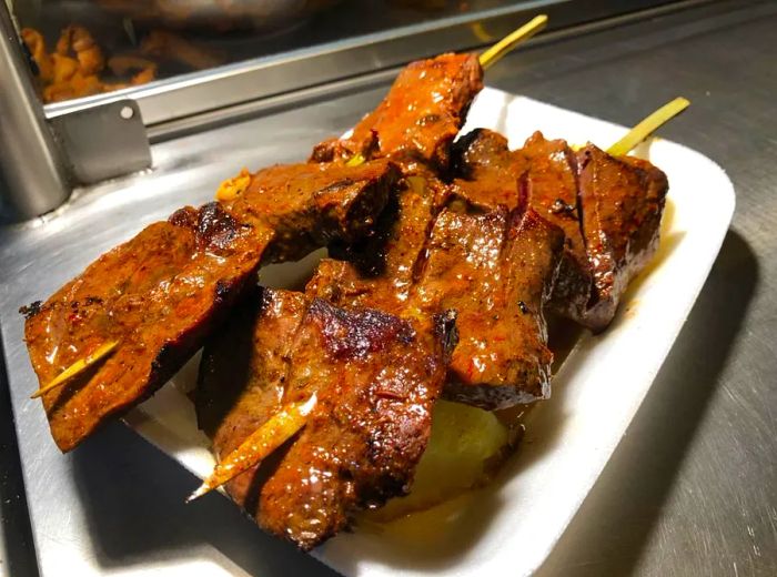 Two skewers of succulent grilled beef gleam on a white paper plate set on a steel counter.