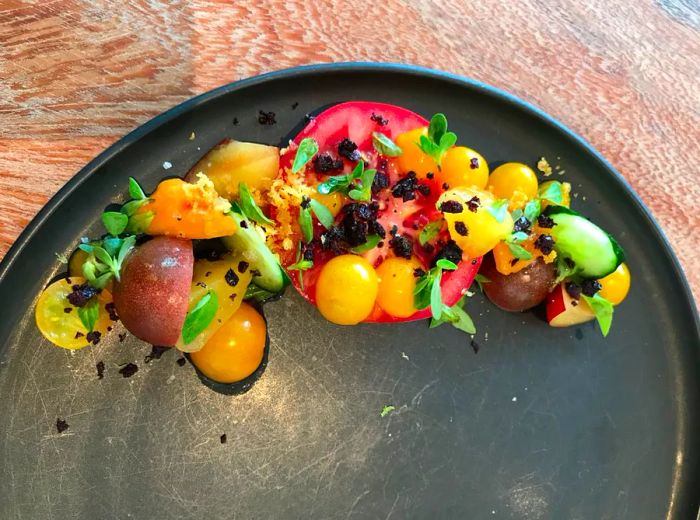 An overhead view of a meticulously arranged tomato salad with assorted herbs and garnishes, artistically placed along one side of a round plate.