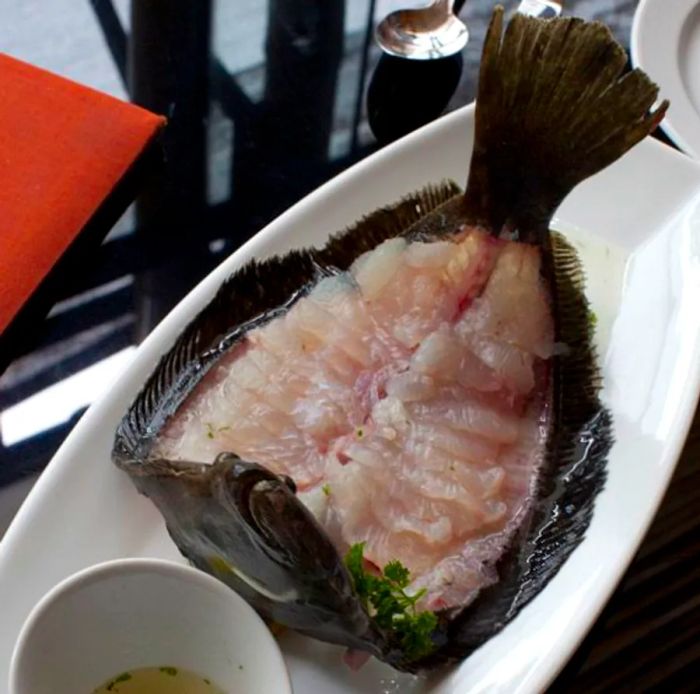 A fish is neatly filleted and arranged on a platter, accompanied by a small bowl of dipping sauce.