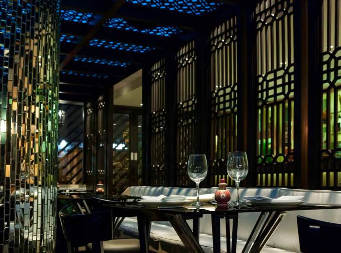 The dim and sophisticated interior of Chifa Titi, featuring a small table with wine glasses in the foreground, tall ornate windows, and sparkling, crystal-like decor.