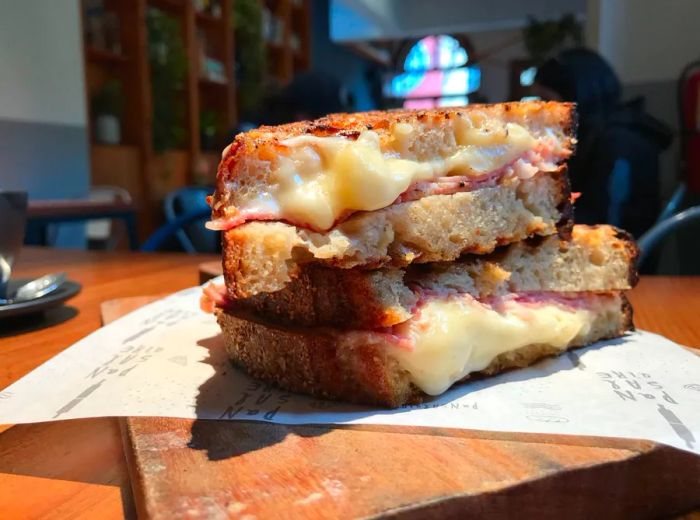 A ham and cheese sandwich, neatly cut in half and stacked with the sliced edges facing the camera, showcasing generous layers of cheese on the exposed sides.