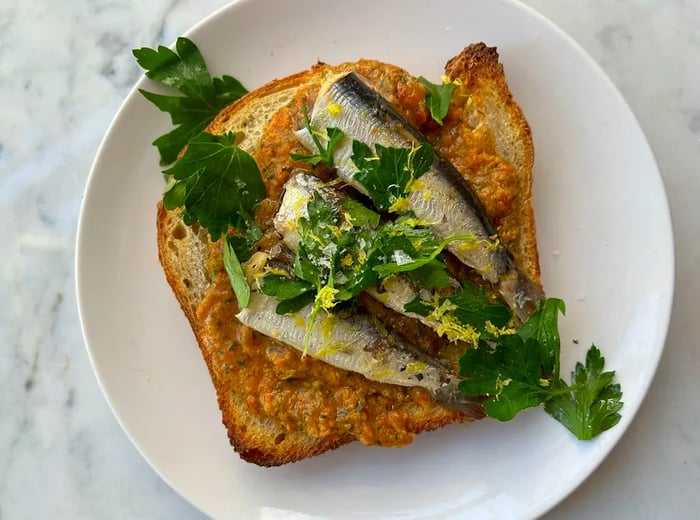 Aerial view of sourdough toast topped with sardines and herbs.