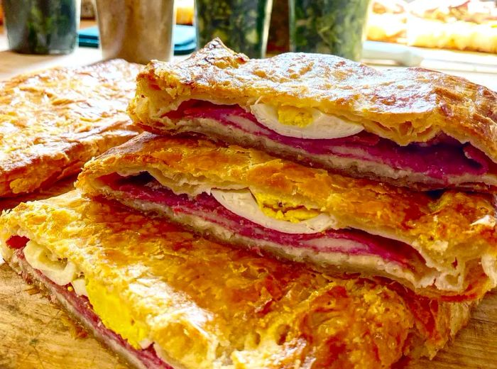 A collection of savory pastries filled with boiled egg and meat, arranged on a wooden counter.