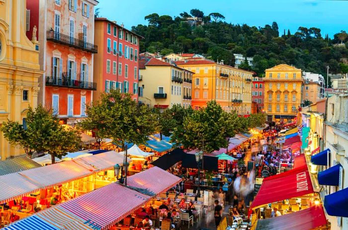 A charming evening scene of colorful buildings and outdoor restaurants in Nice, France.