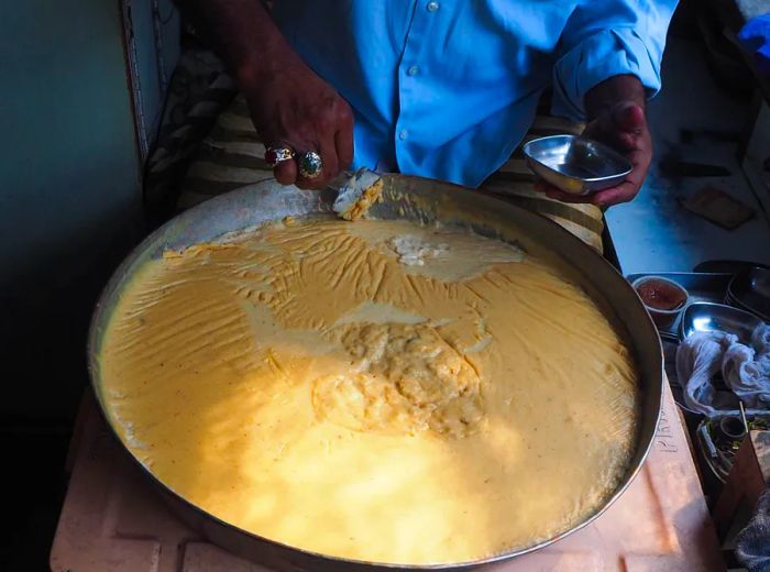 A vendor ladles a delicate portion from a giant vat of kheer into a small bowl.