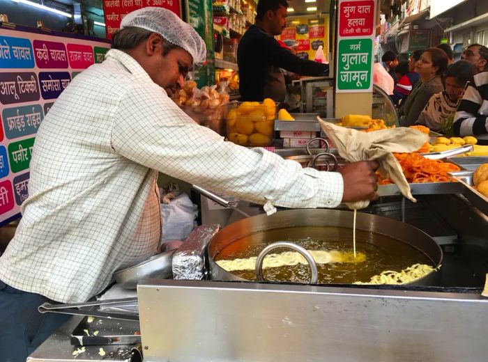 A vendor swirls batter into a pan of hot oil to create crispy, golden jalebis.