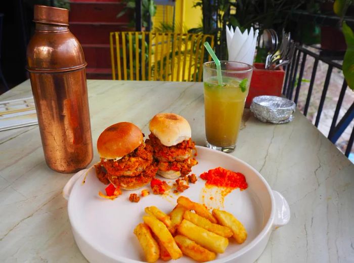 A casual patio scene features two messy sliders with fries on a table, accompanied by a glass of iced tea with a bendy straw and a cocktail shaker.