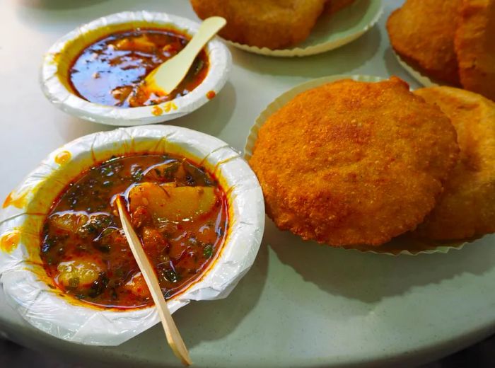 Paper bowls filled with hearty stews of spiced potatoes, accompanied by stacks of crispy kachoris.