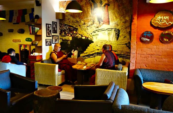 Three patrons enjoy their drinks around a compact coffee table, with a wall adorned with a mix of large and small artworks in the background.