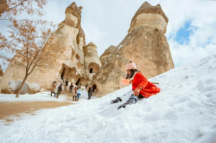 A young girl enjoys sliding down snow-covered fairy chimneys in Cappadocia.