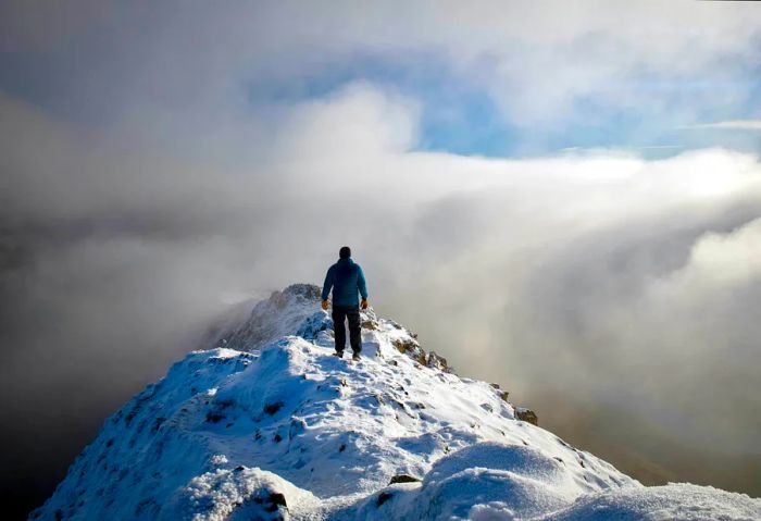 A solo hiker stands above the clouds at Snowdonia's peak, Wales, United Kingdom