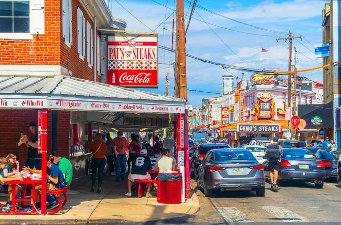 A bustling street corner with Pat's King of Steaks on one side and Geno's Steaks further down the road