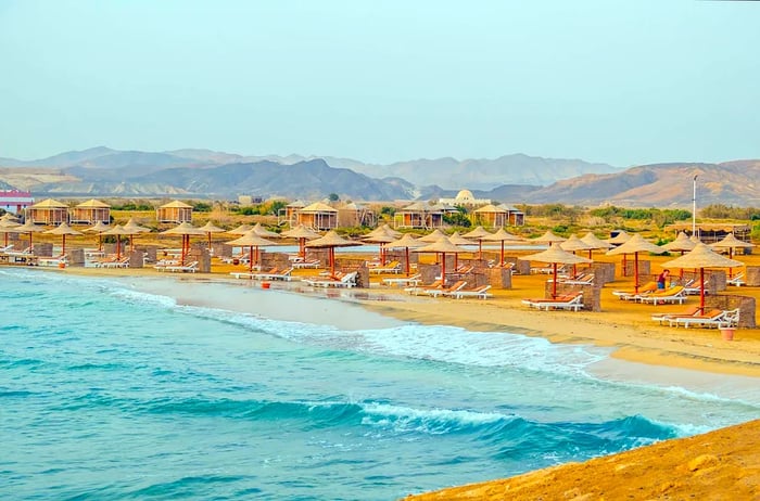 Beach loungers and umbrellas set against a backdrop of orange mountains and turquoise waters in Marsa Alam, Egypt.