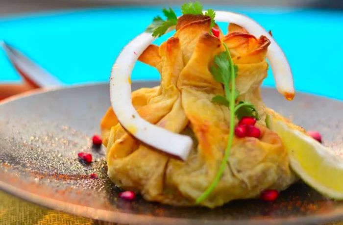 A flatbread dumpling adorned with herbs, onions, and pomegranate seeds.