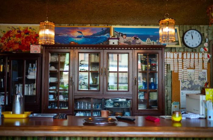 A dark wooden cabinet displaying dishes behind the counter in a typical kissa