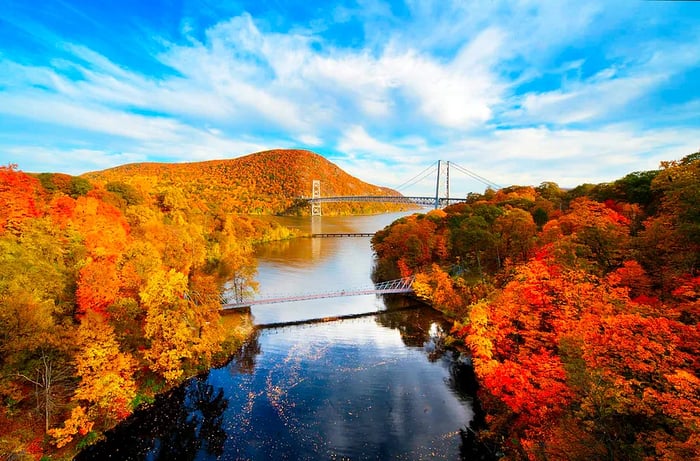 A river meanders through vibrant autumn foliage, with a bridge visible in the distance.