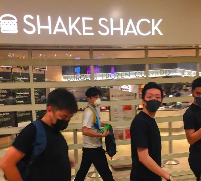 Four masked protesters walk past a Shake Shack sign.