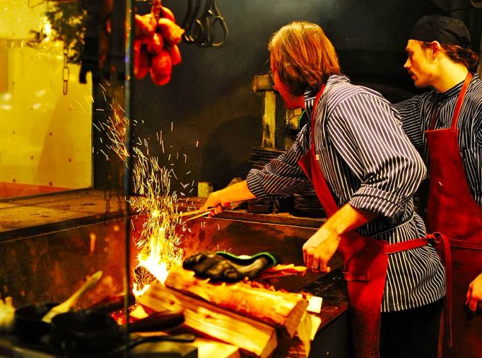 Cooks are tending to ingredients over an open-flame fire pit.