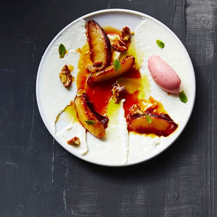 Slices of stewed peaches served on a plate alongside cream, vibrant ice cream, and decorative garnishes.