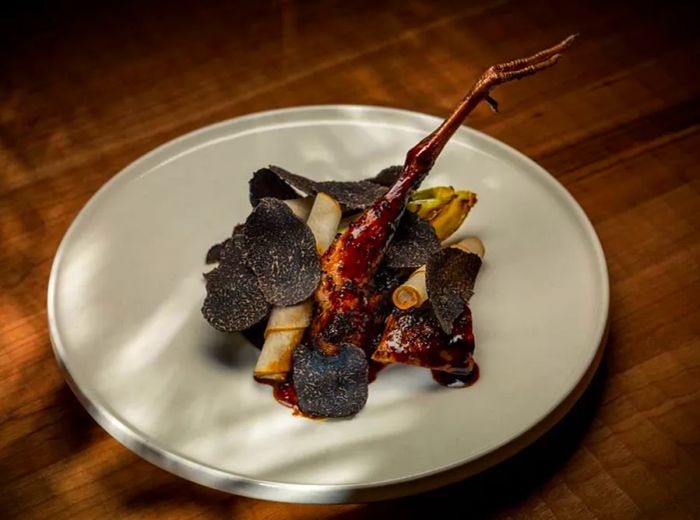 A roasted chicken leg peeks out from beneath a mound of shaved black truffles and assorted vegetables.