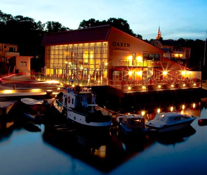 A waterfront building featuring large, illuminated glass panels on one side, with boats docked nearby.